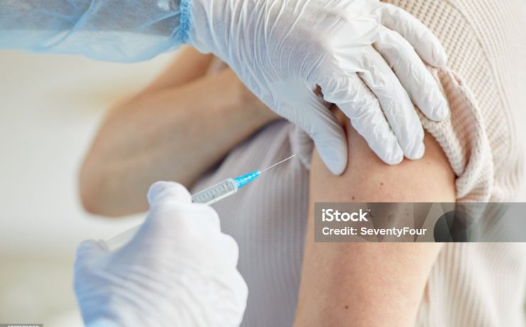 Close-up shot of unrecognizable doctor wearing latex gloves giving Covid-19 vaccine injection into womans shoulder