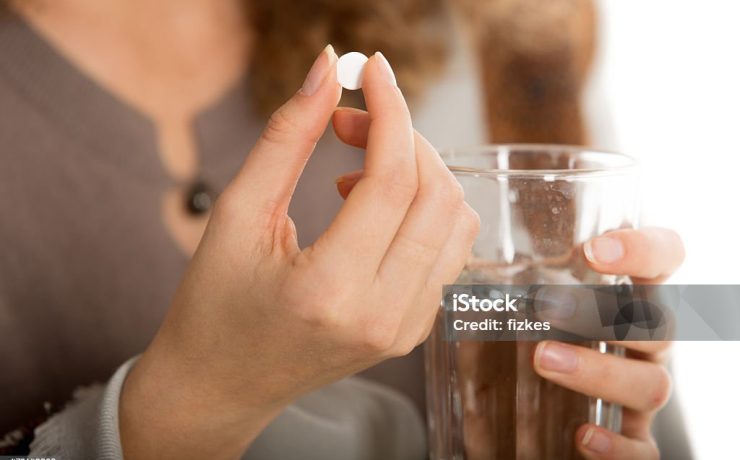 Female hands hold one pill and glass of water close-up